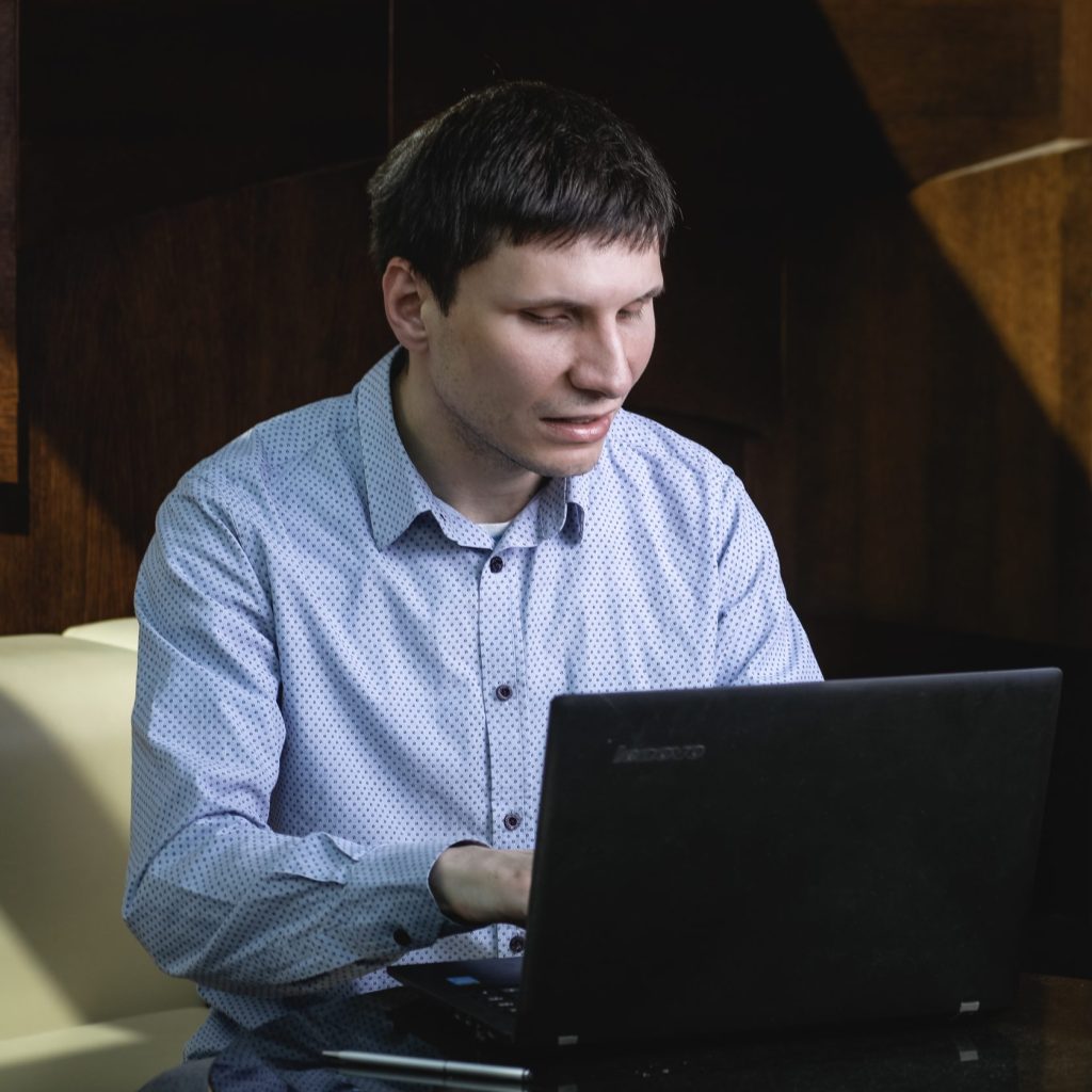 Lazar, a blind man, wearing a blue button down shirt and using his laptop.