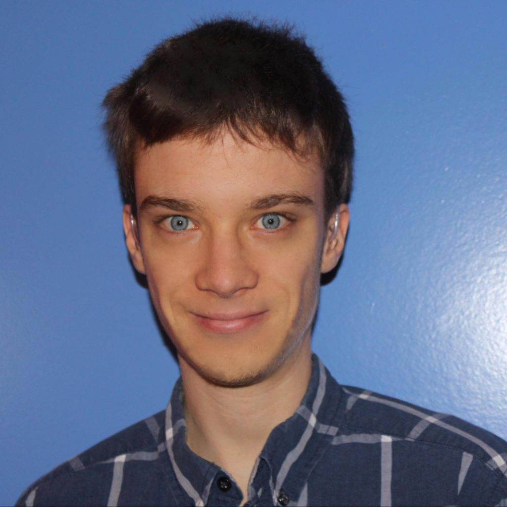 Gregory is a young man with piercing blue eyes. He is wearing hearing aids.
