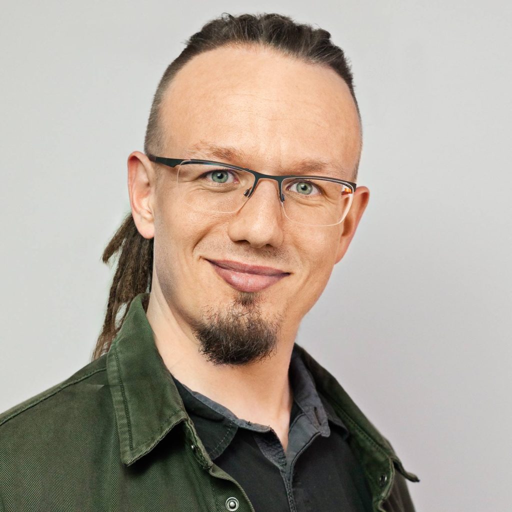 Maciek is a white man in his 30's with dreadlocks, glasses and smile.