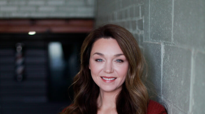 Jessi Conoyer is a white woman in her 30's with long brown hair and blue eyes.