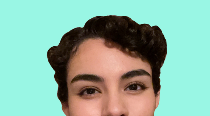 Tanya Piña is a Mexican-American person wearing a smile and a burgundy shirt. They have short, curly brown hair and brown eyes.