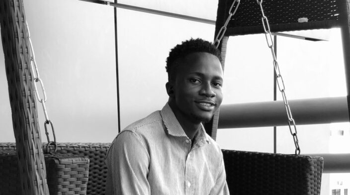 Tobi a dark skin tall guy with full hair, seating with a beaming smile