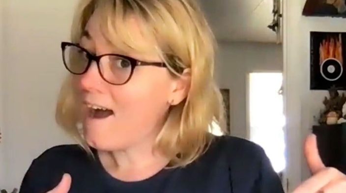 AmyJune Hineline: a woman with glasses pointing to a logo on her tshirt
