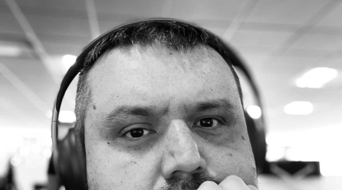 A black-and-white portrait of Norbert Rum with headphones, resting his chin on his fist, wearing a collared shirt.