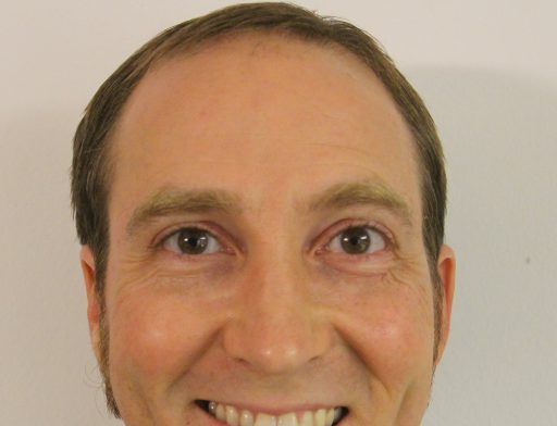 Deneb Pulsipher, a brown-haired, brown eyed man with sideburns smiling at the camera
