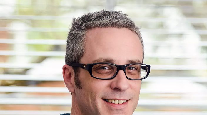 Jonny Allbut is a white male in his late 40's with short greying hair and glasses, wearing a blue checked shirt.