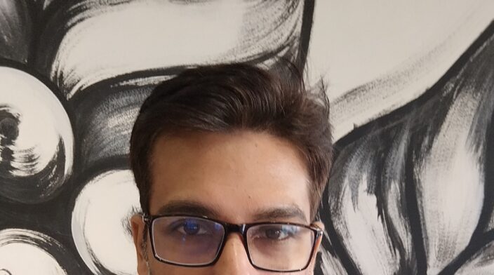 Anam is a South Asian man in his 30s with short black hair and a neatly trimmed beard