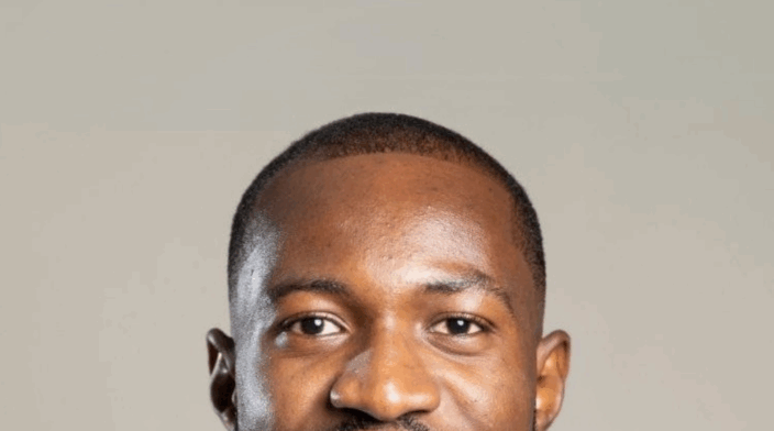 Samuel Osei is a dark skin man with a short hair and a smile, wearing a white t-shirt.