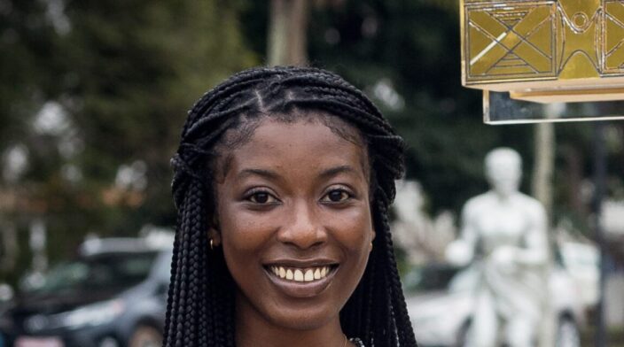 Madlin Akua Nti is a dark-skinned woman in her early 20s with long black braids and a broad friendly smile.