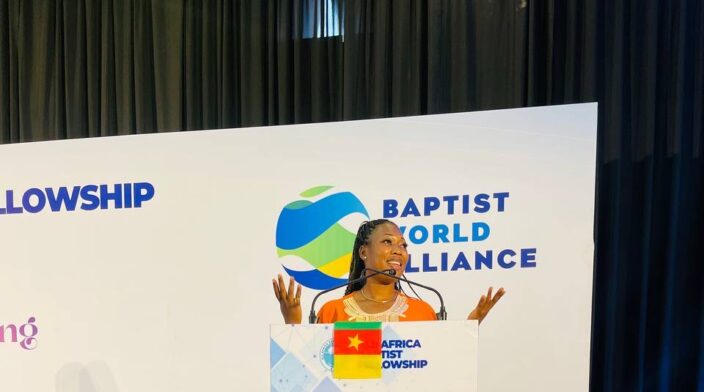 A photo of me in an orange dress speaking at the baptist world alliance conference which held in Rwanda Africa.