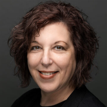 Close up of Sharon Rieger, a woman with short dark brown wavy hair smiling at the camera