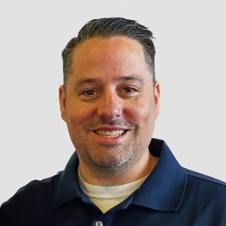 Steve is a light-skinned man with short, dark hair brushed back, neatly trimmed salt-and-pepper facial hair, and a friendly smile. He is wearing a navy-blue polo shirt and is photographed from the shoulders up against a plain light-gray background.