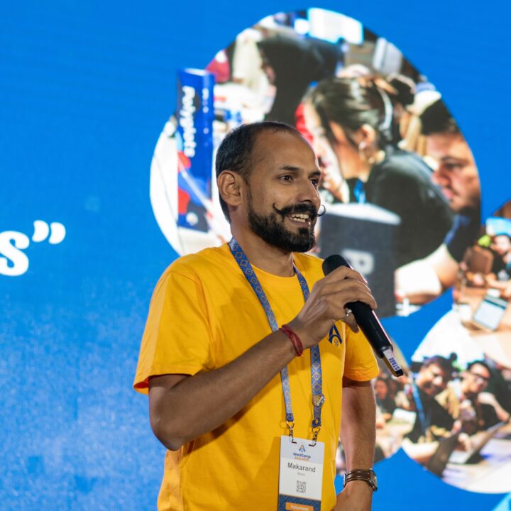 Makarand Mane speaking at WordCamp Asia 2025 in Manila, Philippines, with a smile, holding a microphone on stage.