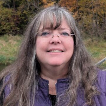 Louise Saletta is a white woman with long brown hair, glasses and a friendly smile.