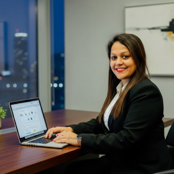Sonali is a woman in her 30s with medium-brown skin, long dark hair, and a warm, friendly smile. She is wearing a professional outfit and is looking confidently at the camera.