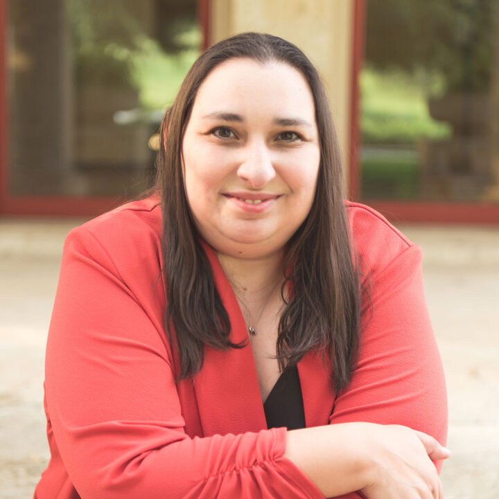 Cousett Known As Techie Mamma a Latina sits on some steps with a bright smile.